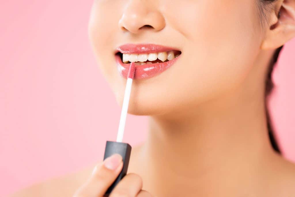 A woman putting on gloss lip liner on her lips 