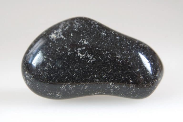 An up close photo of a black onyx stone on a pale gray background, What Does Black Onyx Jewelry Mean?
