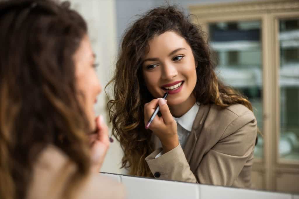 Businesswoman is applying lipstick while preparing for work