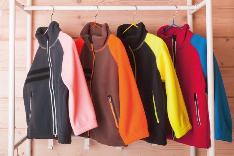 Colorful fleece jackets are hanging on hangers near wooden wall in a rack. 9 Types Of Fleece You Should Know