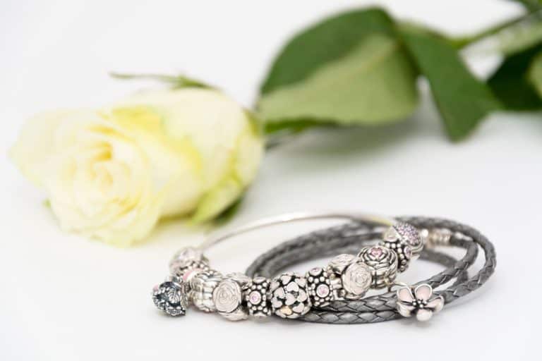 Two beautiful Pandora bracelets combined of different charms (beams) on white background next to a beautiful rose, How Many Charms Fit On A Pandora Bracelet? [By Type Of Bracelet]