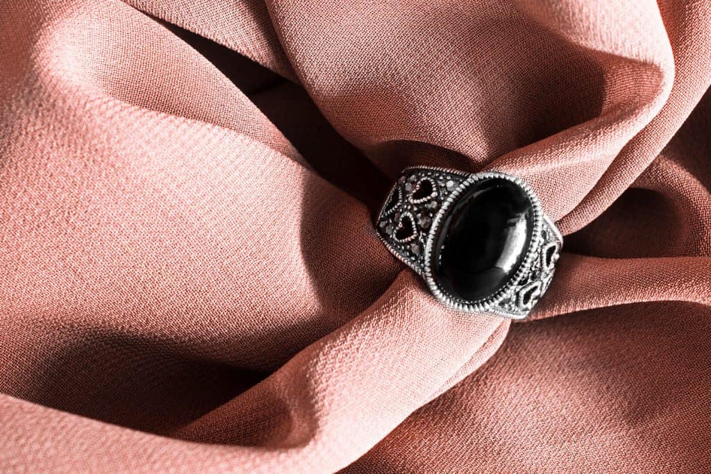 Винтажное кольцо с черным ониксом на мятом бежевом шелке в качестве фона