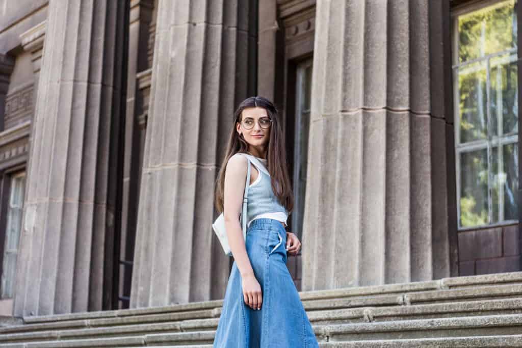 A beautiful woman posing on the stairs wearing a denim skirt and a small handbag