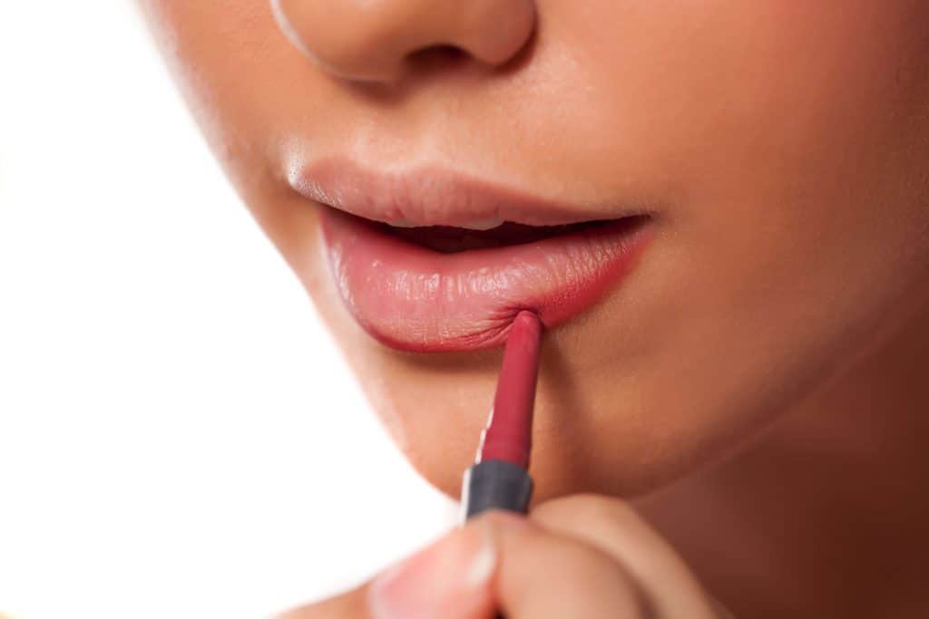 A woman applying a red lip liner on a white background
