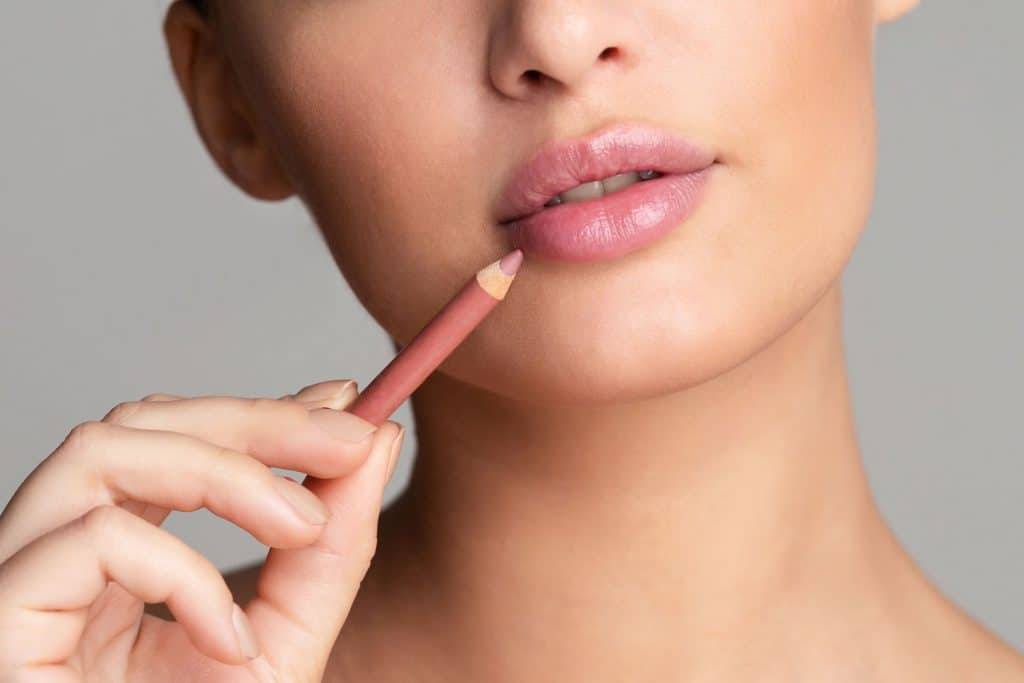 A woman drawing her lips on a pink nude lipstick