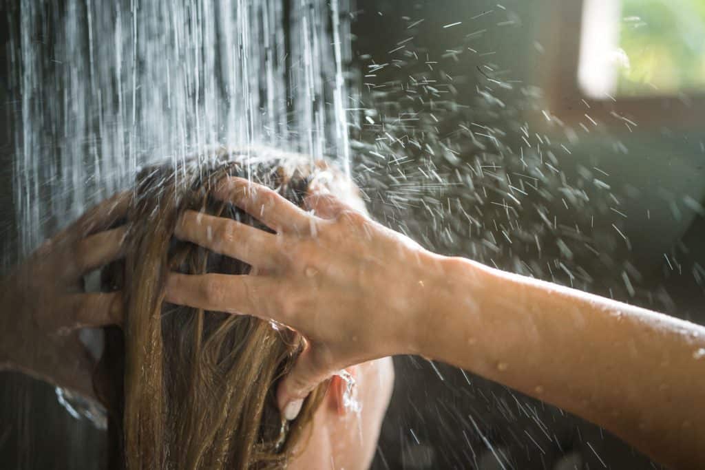 A woman washing her hair under a soothing shower bath