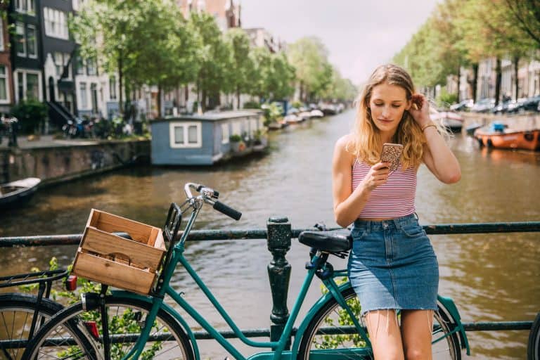 A woman wearing a pink shirt and denim pants on the bridge on Amsterdam, What To Wear With A Denim Skirt [17 Awesome Looks]