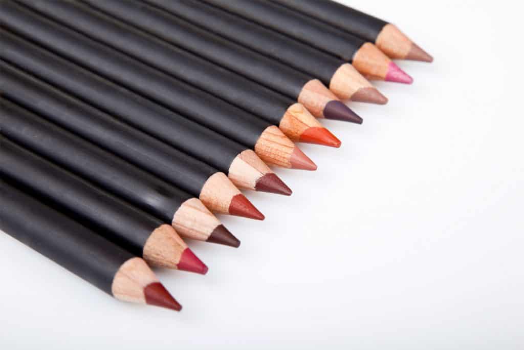 Different colored make up pencils on a white background