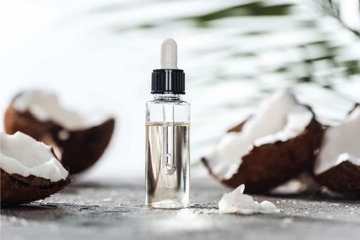 Selective focus of glass bottle with coconut serum and dropper near cracked coconuts