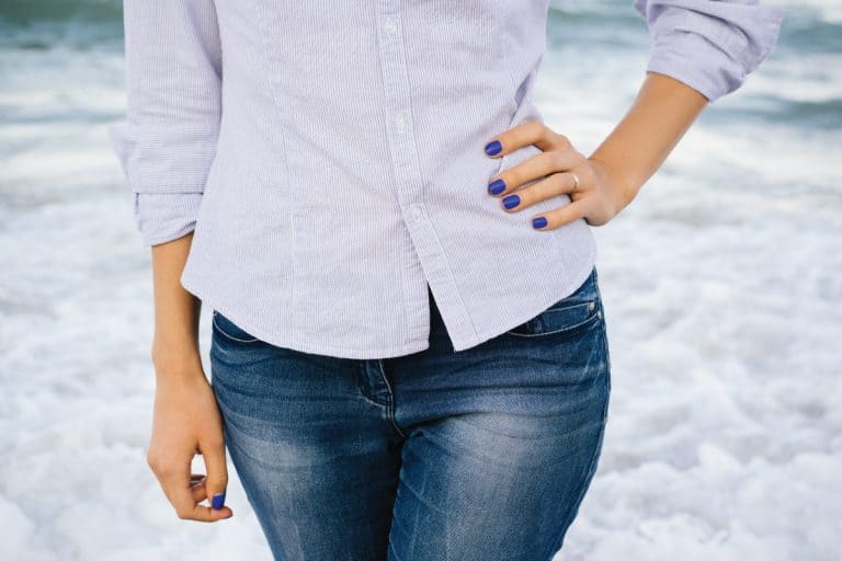 Woman in faded jeans and shirt standing in the sea foam on the beach. 4 Methods To Fade Jeans