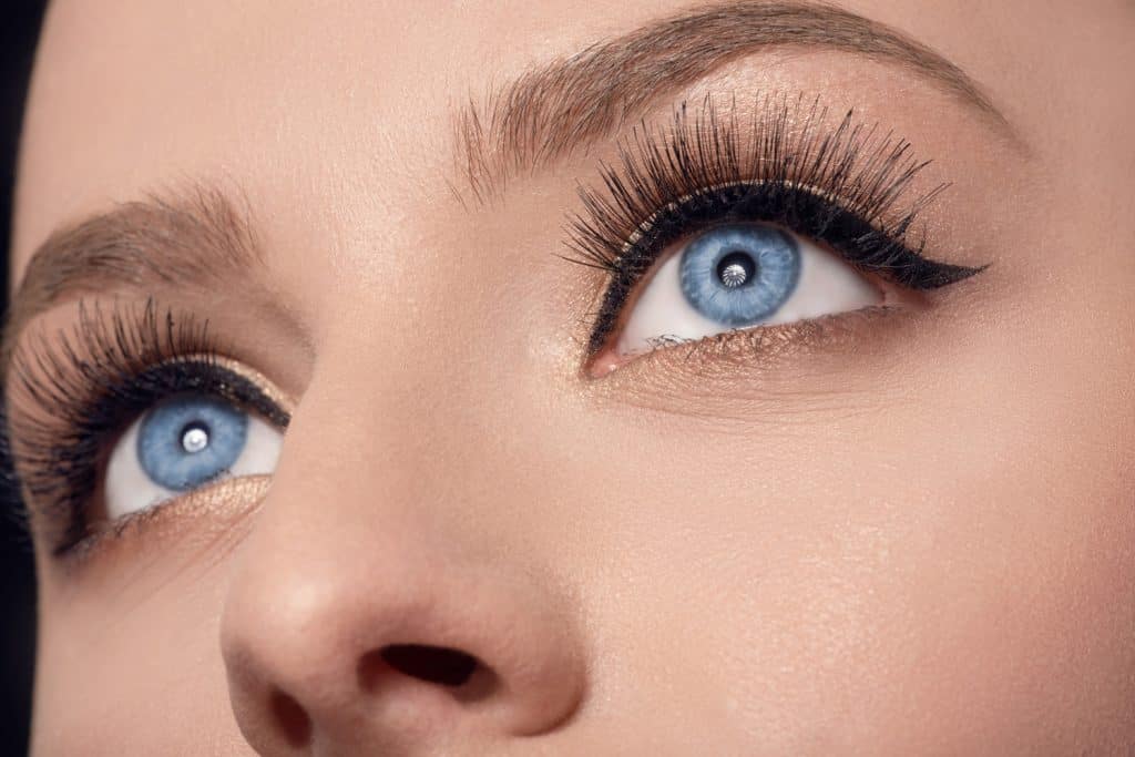 close-up shot of beautiful blue eyes of woman looking up, black eyeliner and mascara makeup.