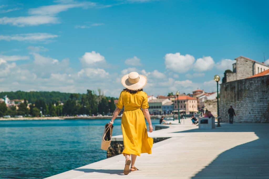 woman walking by sea quay in summer day in yellow sundress. summer vacation