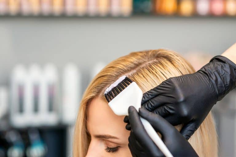 A blonde woman putting on hair dye on her hair at a salon, Does Hair Dye Or Developer Expire?
