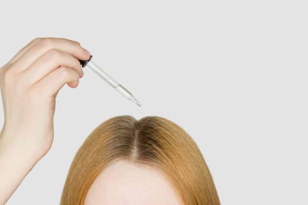 A glass pipette with a hair growth agent is applied to the parting of the hair, red hair