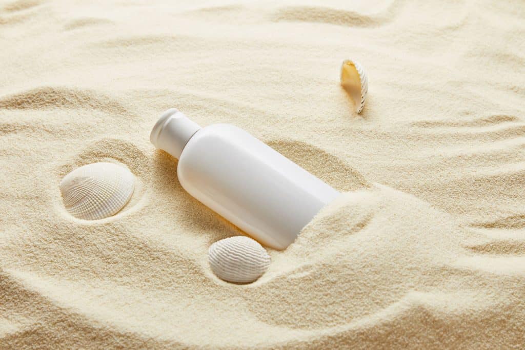 A sunscreen placed on the beach sand placed next to shells