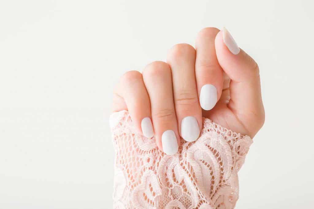 Красивая ухоженная рука женщины с белыми ногтями на светло-сером фоне