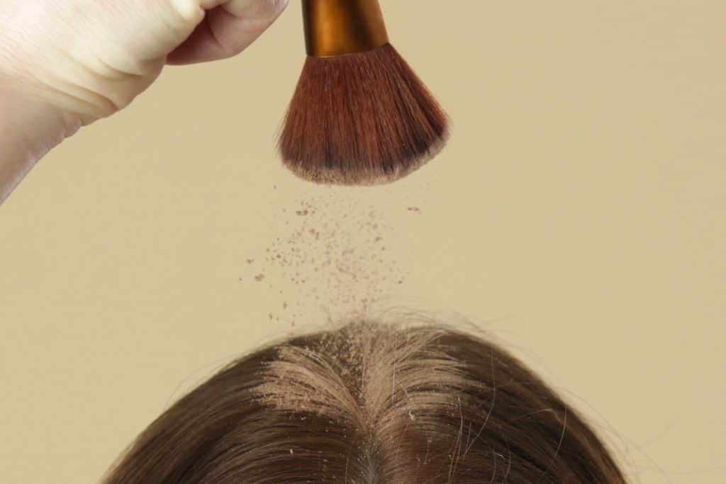 Крупным планом вид женщины, наносящей натуральный сухой шампунь на корни волос