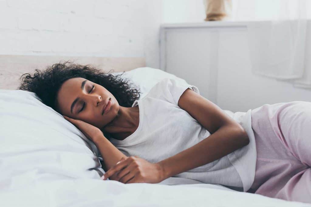Pretty African American woman in pajamas sleeping on white bedding
