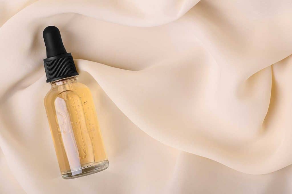 Serum for skin care in a glass bottle with a pipette on a silk cloth