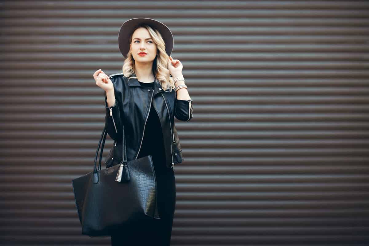 Street portrait of glamour sensual young stylish lady wearing trendy fall outfit. Blonde woman in black hat and leather jacket and bag