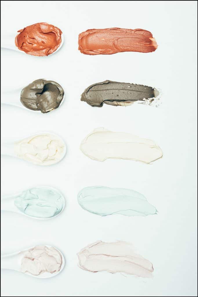 Top view of spoons and various colorful clay mask smudges placed in row isolated on white surface