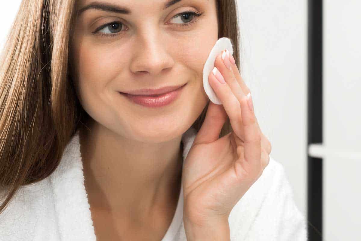 Woman cleaning face with cotton pad, How To Remove Sunscreen From Your Face - Even Without Cleanser