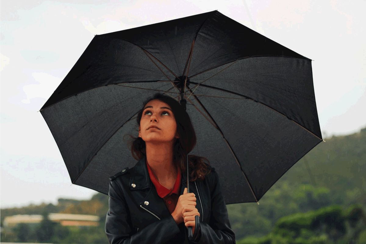 Young woman with a leather jacket holds open black umbrella in his hand under the rain