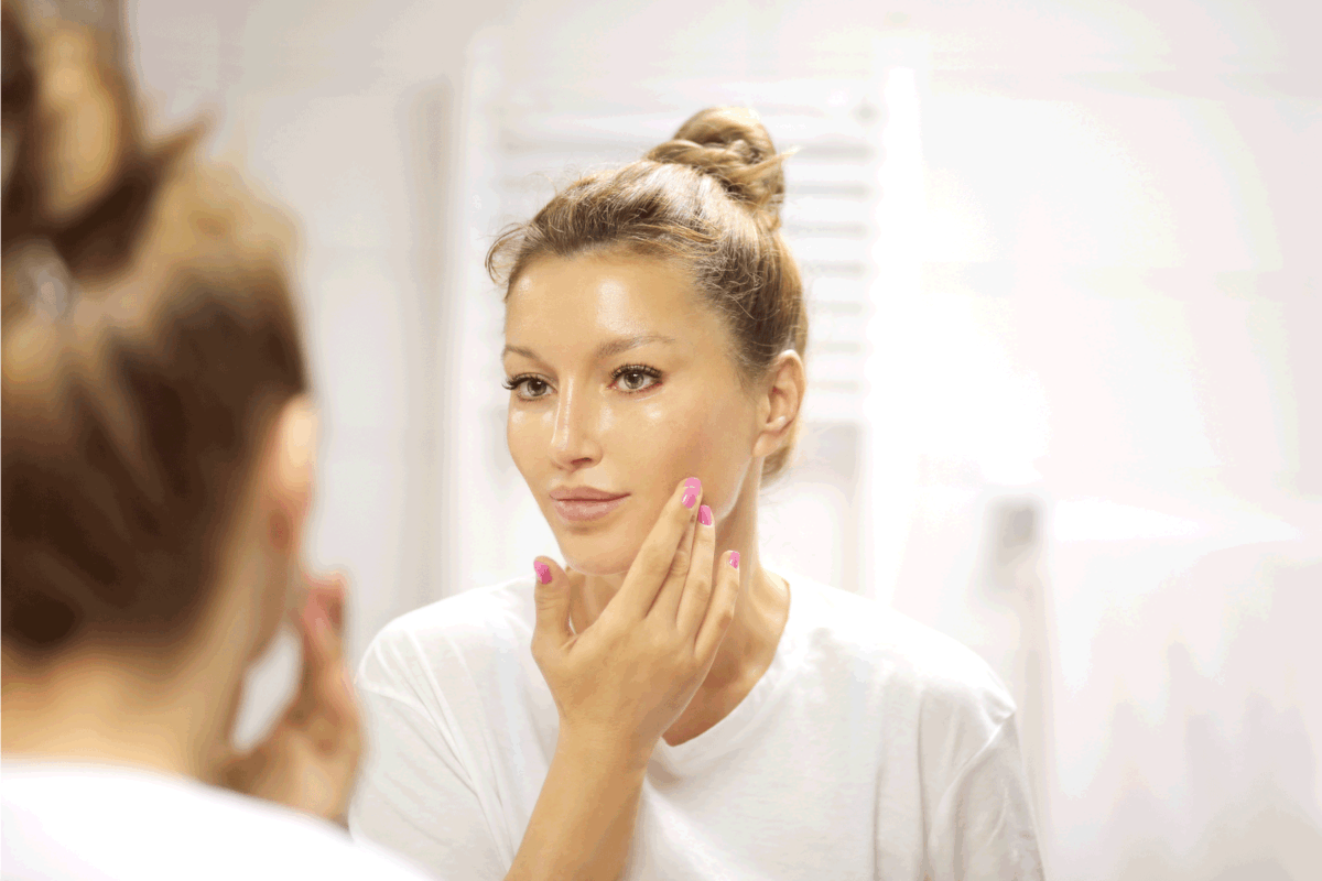 woman applying moisturizing cream onto face infront of mirror