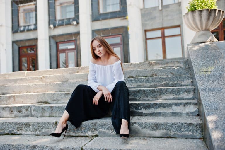 A beautiful woman sitting on the stairs wearing a white long sleeve shirt and black palazzo pant, What Top To Wear With Palazzo Pants [6 Great Options]