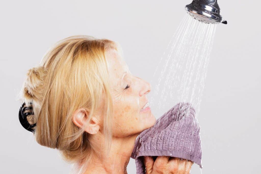 A mature woman standing in a shower.