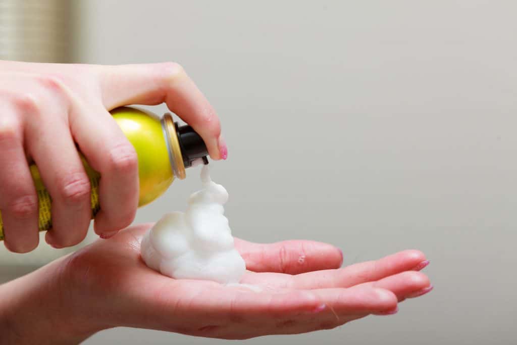 A woman spraying hair mousse on her hand