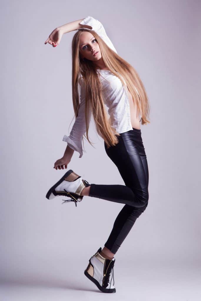 A woman wearing a white long sleeve shirt, black leggings, and white high heel shoes