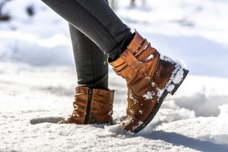 An up close photo of a woman wearing boots while walking on the snow