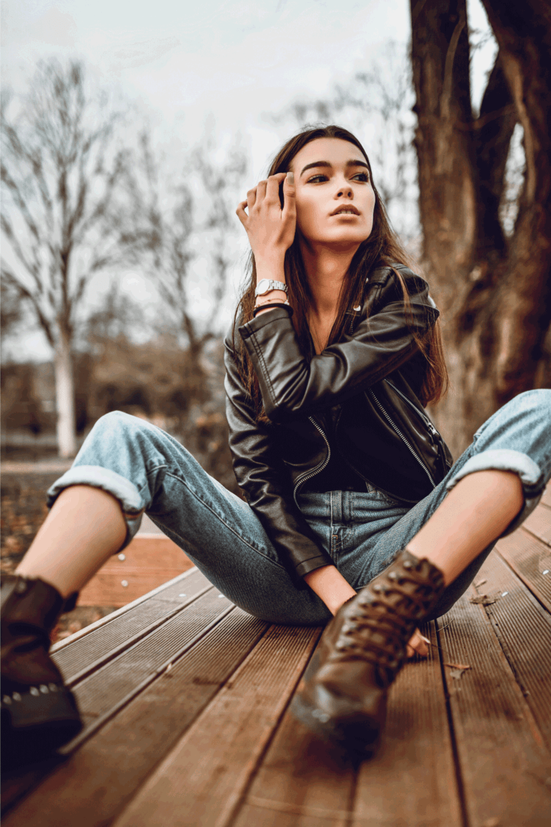 Beautiful Female Sitting On Bench In The Park wearing leather jacker and boots