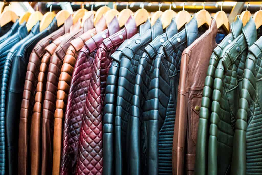Close up color image depicting handmade leather jackets in a variety of different colors hanging up in a row on the rail