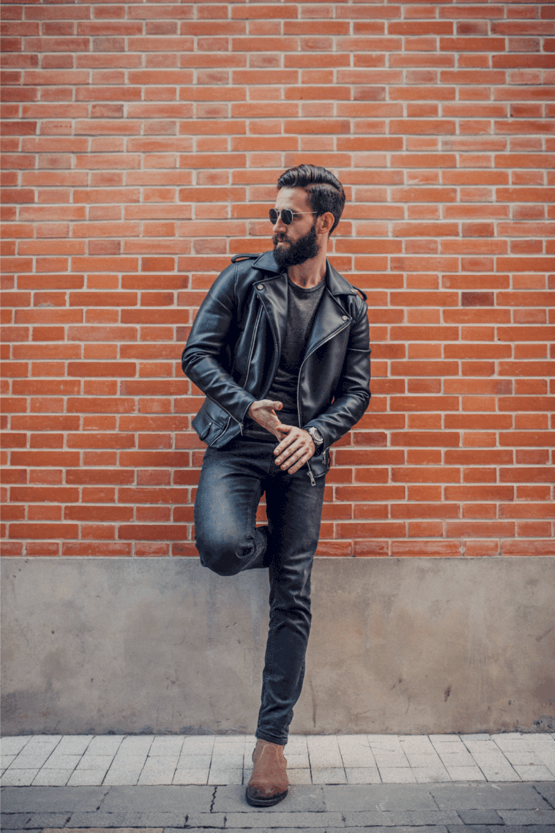 Handsome young man posing outdoors wearing leather jacket and leather boots