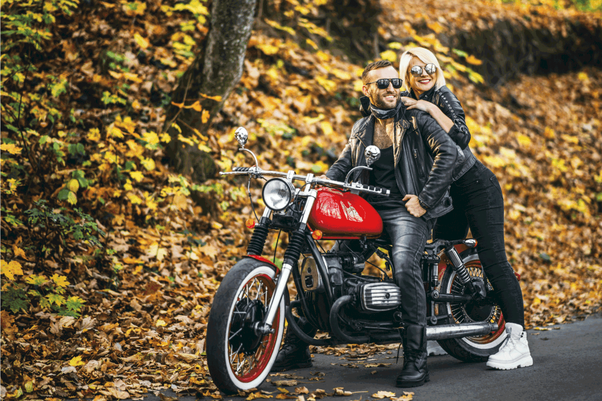 Pretty couple near red motorcycle on the road in the forest wearing leather jackets