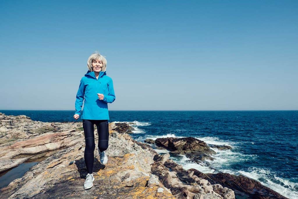 Senior woman jogging on a rocky coastline