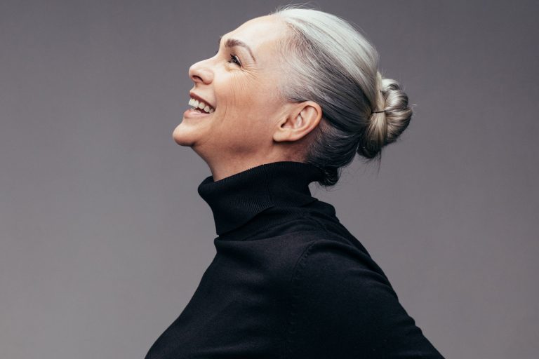Side view of senior woman laughing on gray background. Profile view of mature woman in black casuals looking happy, Does Electrolysis Work On White Or Gray Hair?