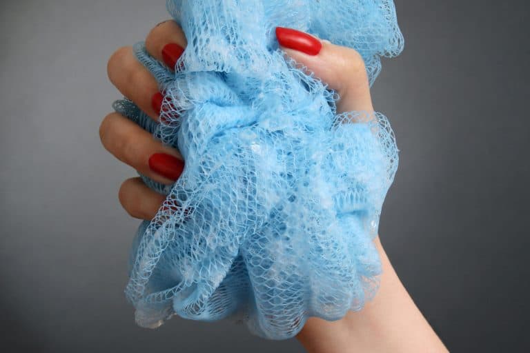 Woman hand holding blue loofah isolated in black background, How Long Should You Keep A Loofah? [The Answer Might Surprise You!]