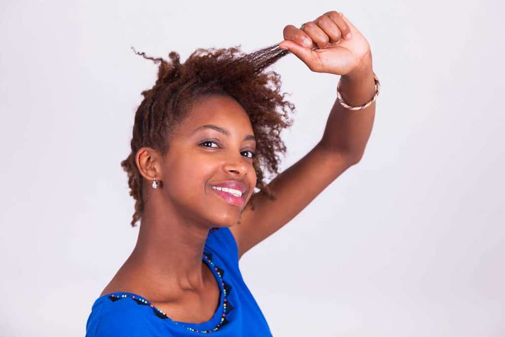 Молодая афроамериканка заплетает вьющиеся афро-волосы косы