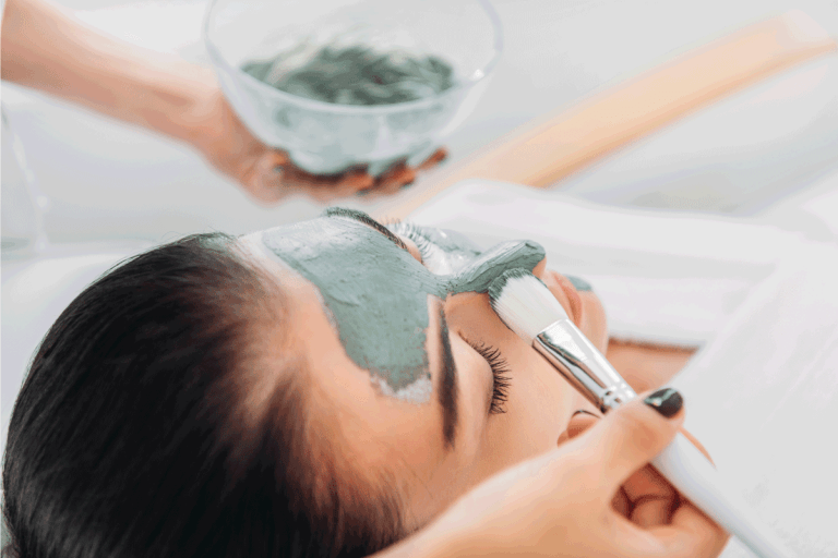 cosmetologist applying clay mask with brush on female face in spa salon. How Often Should You Use An Aztec Clay Mask