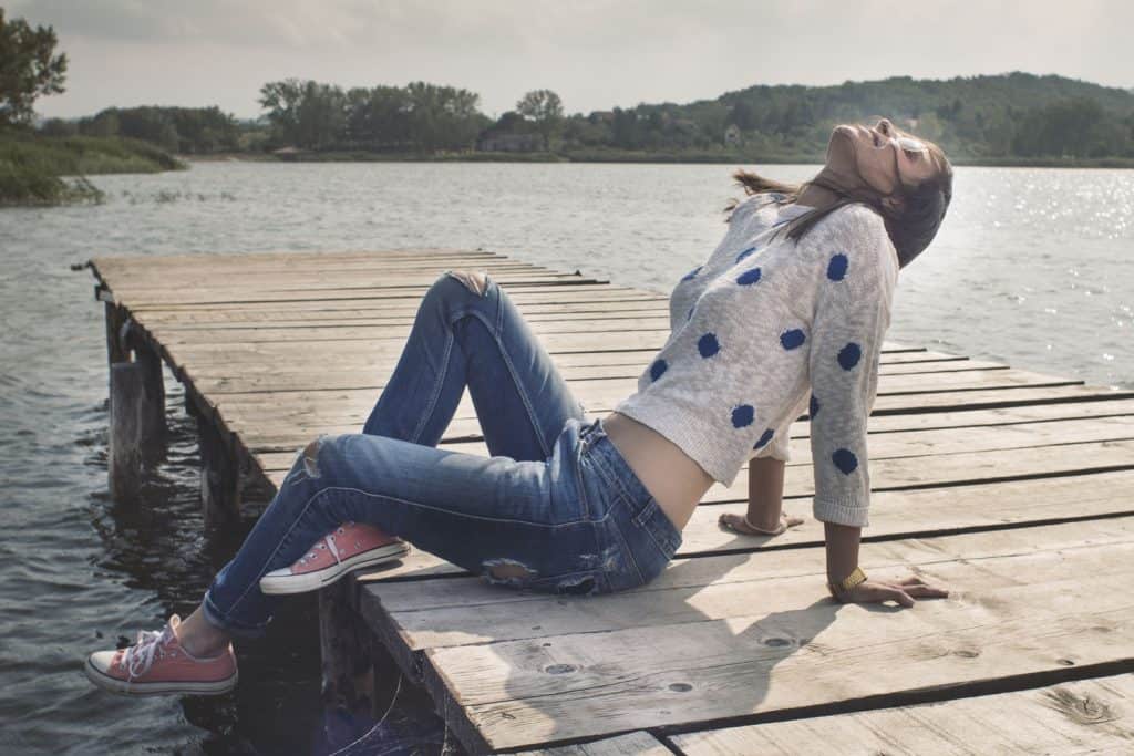 A beautiful woman posing on the dock of a lake wearing a dotted blouse and skinny jeans