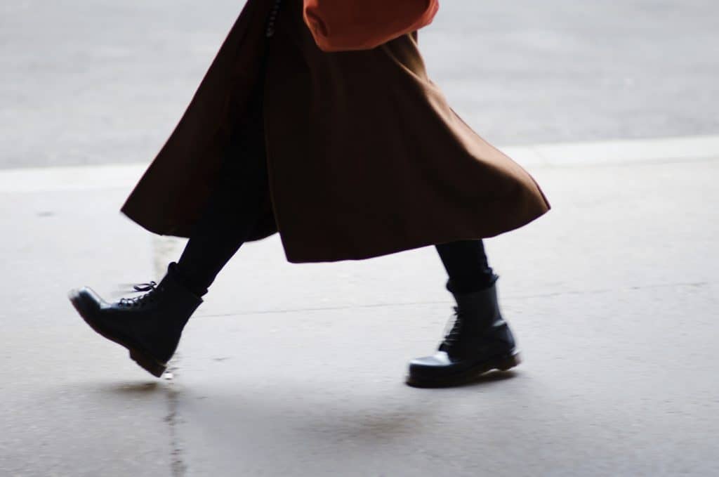 A fashionable woman wearing a long winter coat and thick funky boots walking by on the city streets