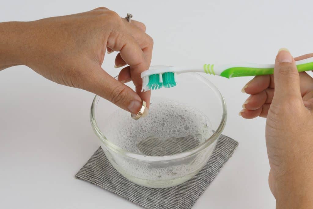 Серебряное кольцо чистится зубной щеткой в ​​мыльной воде.
