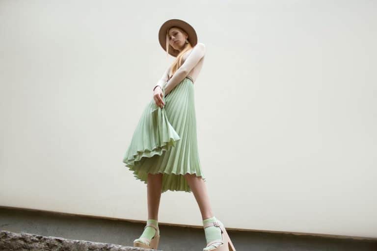 A tall beautiful woman wearing a green skirt, beige sweater, and a sun hat, How To Hem A Pleated Skirt [Even Without Sewing!]
