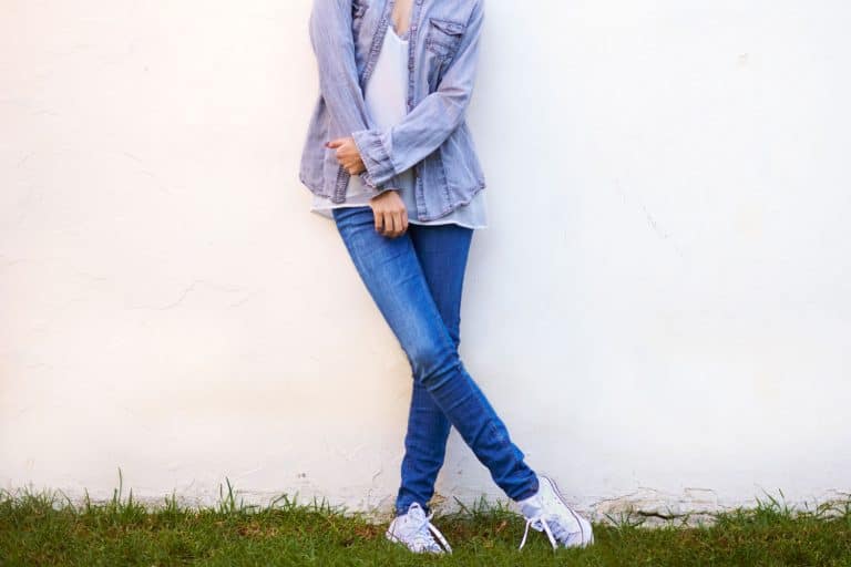 A tall beautiful woman wearing skinny jeans, white sneakers, and a denim jacket, What Sneakers To Wear With Skinny Jeans?