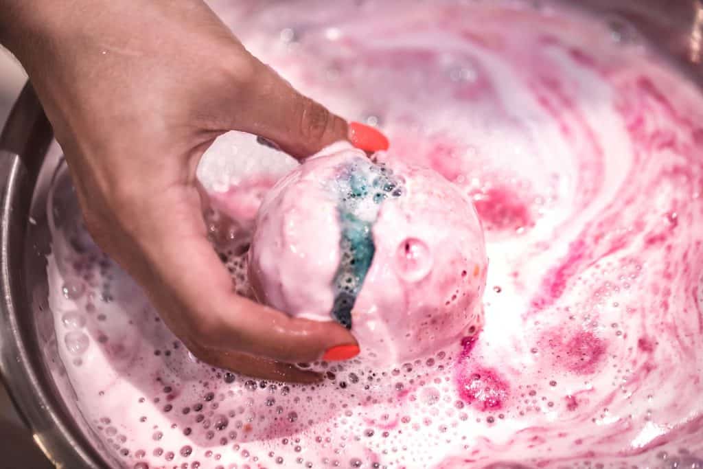 A woman dipping a pink colored bath bomb