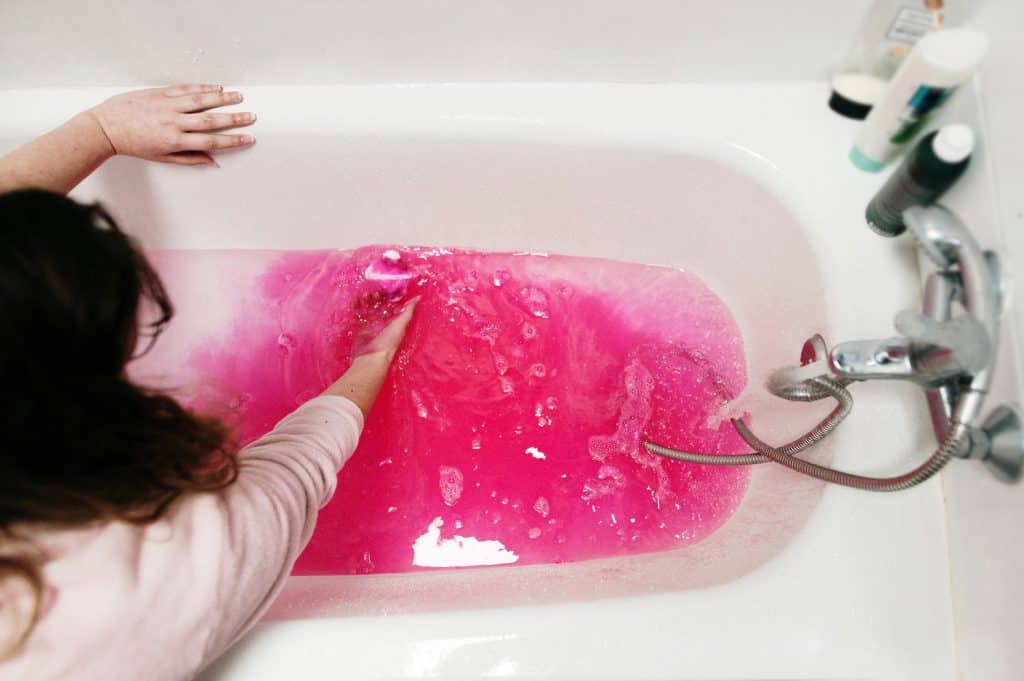 A woman putting a pink bath bomb in the water in a bathtub