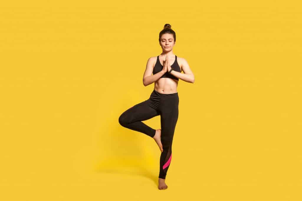 A woman doing a standing meditation on a yellow background